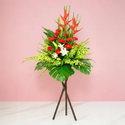 A Vibrant Flower Arrangement On A Stand Featuring Red And White Gerberas, Casa Lilies, Orchids, And Seasonal Greenery.