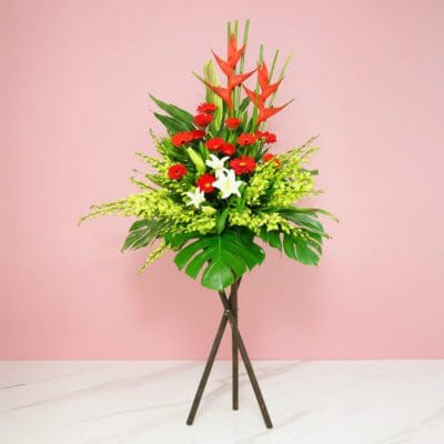 A Vibrant Flower Arrangement On A Stand Featuring Red And White Gerberas, Casa Lilies, Orchids, And Seasonal Greenery.