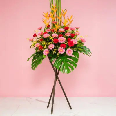 Colorful Flower Arrangement With Heliconia, Gerberas, And Roses Displayed On A Stand In Front Of A Pink Wall.