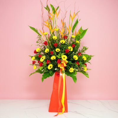A Floral Arrangement Featuring Heliconia, Gerberas, And Roses Displayed On A Pink Background.