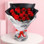 A bouquet of vibrant red roses elegantly arranged in a polished marble vase.