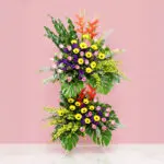 A Large Floral Display With Gerbera, Roses, Orchids, And Seasonal Greenery Set Against A Pink Backdrop.