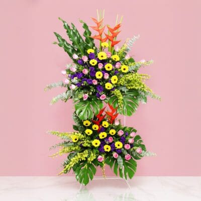 A Large Floral Display With Gerbera, Roses, Orchids, And Seasonal Greenery Set Against A Pink Backdrop.