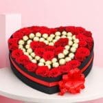 A heart-shaped box filled with assorted chocolates, accompanied by fresh red roses.