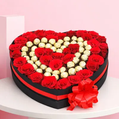 A heart-shaped box filled with assorted chocolates, accompanied by fresh red roses.