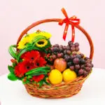 A woven basket filled with colorful fruit and vibrant flowers arranged together.