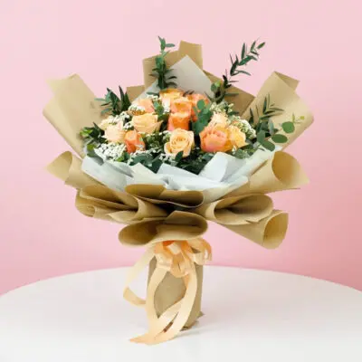 A hand bouquet of 12 peach roses wrapped in brown paper, elegantly arranged for a charming floral display.