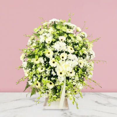 A white floral arrangement on a marble table, serving as a condolence stand.