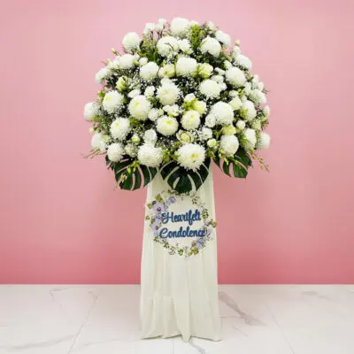 A white funeral flower arrangement beside a sign that reads "Heartfelt Condolence," conveying a heartfelt message.