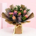 A bouquet of pink and purple roses wrapped in a brown paper bag, symbolizing love and happiness for special occasions.