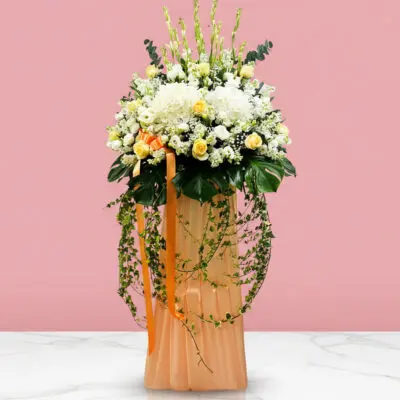 A memorial condolance stand containing white and orange flowers on a vibrant pink backdrop.