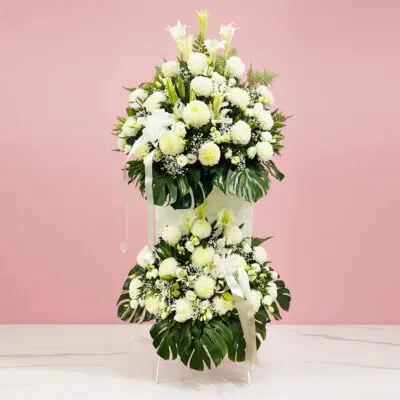 A large white flower arrangement featuring chrysanthemums, elegantly displayed on a pink table, symbolizing comfort and honor.
