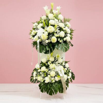 A large white flower arrangement featuring chrysanthemums, elegantly displayed on a pink table, symbolizing comfort and honor.