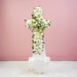 A white cross with colorful flowers displayed on a light pink background.