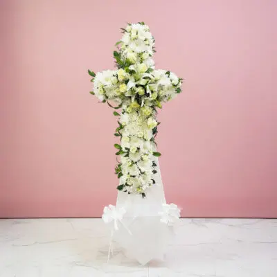 A white cross with colorful flowers displayed on a light pink background.
