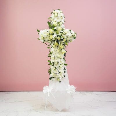A white cross with colorful flowers displayed on a light pink background.