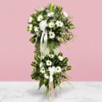 Elegant white floral arrangement of daisies surrounded by lush greenery, symbolizing sympathy and cherished memories.