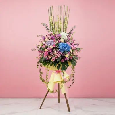 A majestic flower arrangement on a stand, displayed against a soft pink wall.