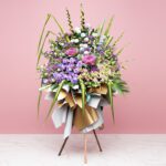 Elegant floral arrangement in purple and pink on a stand, set before a pink wall, ideal for weddings and corporate events.