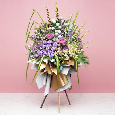 Elegant floral arrangement in purple and pink on a stand, set before a pink wall, ideal for weddings and corporate events.