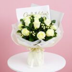A bouquet of white roses with a congratulations card on a wooden table.