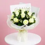 A bouquet of white roses with a congratulations card on a wooden table.