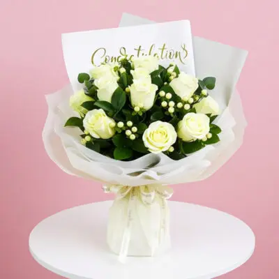 A bouquet of white roses with a congratulations card on a wooden table.