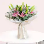 A vibrant bouquet featuring pink lilies surrounded by fresh eucalyptus leaves.