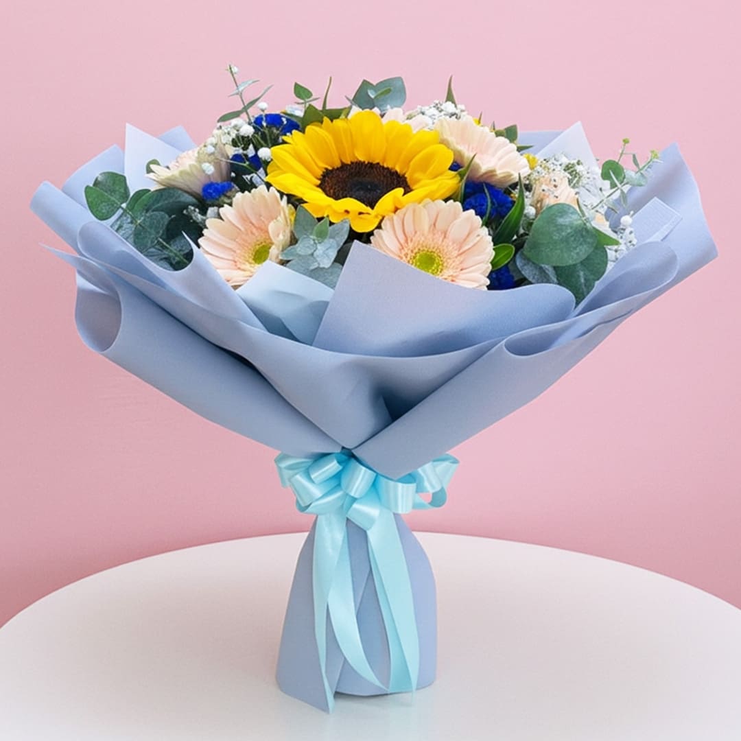 Nature’s Shining Stars-01-569-03 A hand bouquet featuring three sunflowers, pink and purple gerbera, baby breaths, and seasonal greens, tied with a blue ribbon.