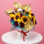 A bouquet of vibrant sunflowers and delicate roses arranged in a white box.