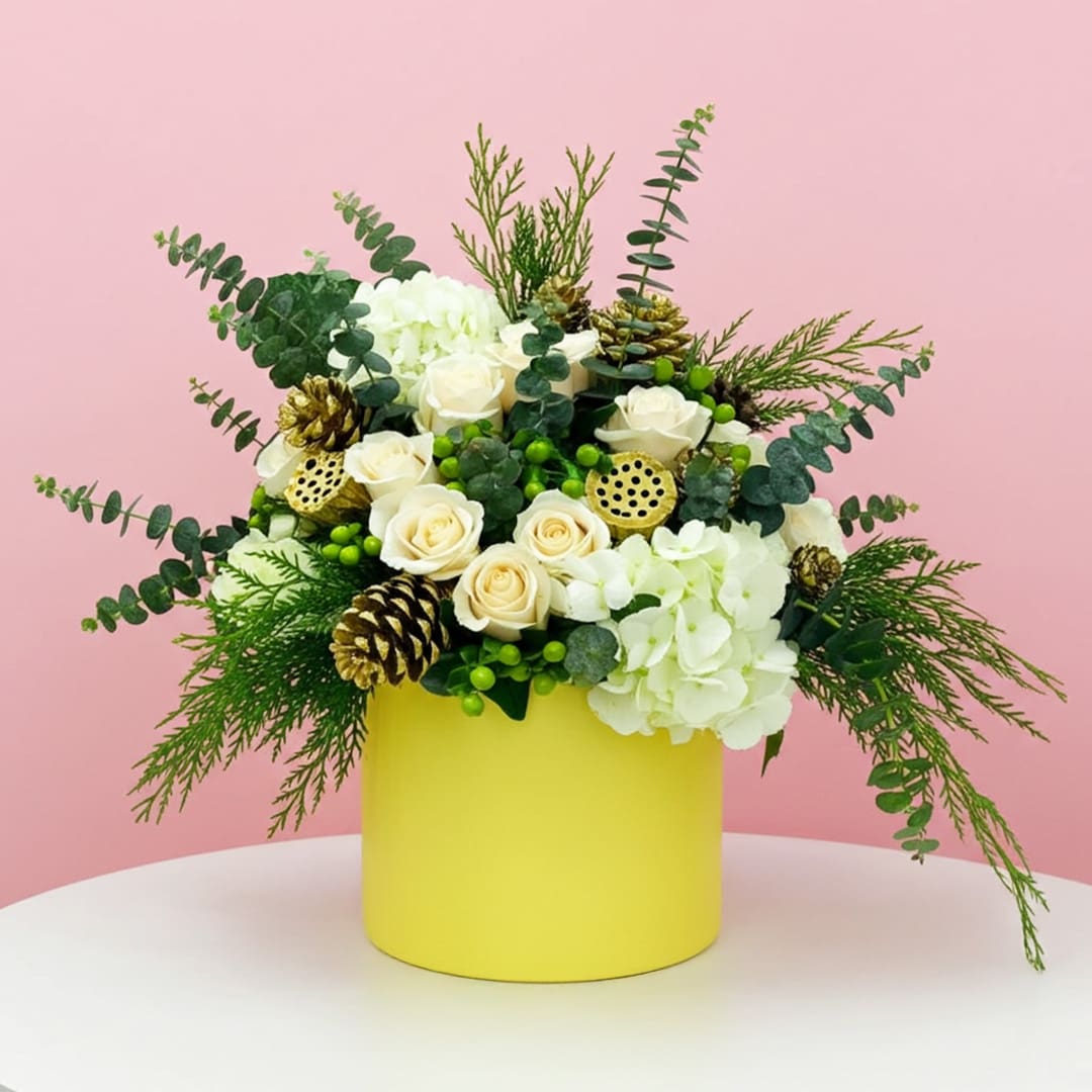 Snowy Petals Ensemble-01 A yellow vase filled with white flowers and pine cones, placed beside a festive Christmas box.