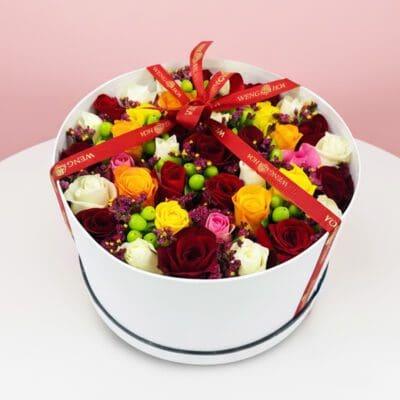 A white gift box tied with a red ribbon, accompanied by a vibrant bouquet of flowers.