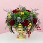 A gold vase filled with red roses, pinecones, and festive decorations, serving as a Christmas centerpiece.