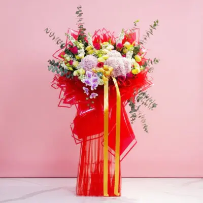 A red vase filled with fresh flowers and a ribbon, set against a soft pink background, symbolizing celebration and new beginnings.