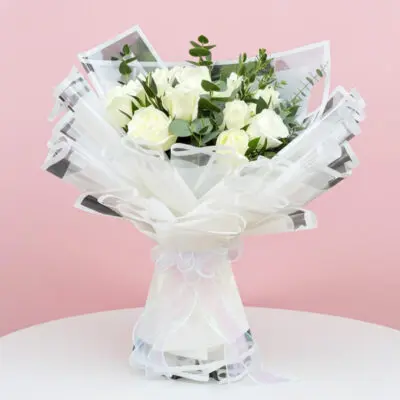 A hand bouquet of ten white roses and eucalyptus in a clear vase, elegantly arranged for a fresh and classic look.