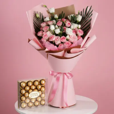 A bouquet of pink roses alongside a box of chocolates on a pink table