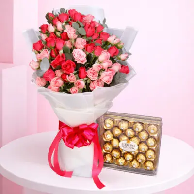 A romantic arrangement of roses and Ferrero chocolates on a table, named Sweetheart’s Ferrero Rose Surprise.