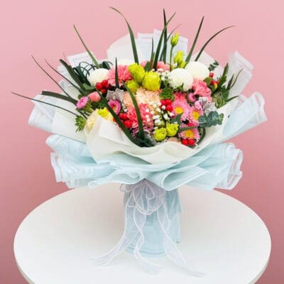 A vibrant bouquet of flowers arranged on a table, set against a soft pink background.
