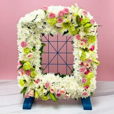 A decorative wreath with pink and white framing set on a pastel pink background, enhancing its charming appearance.