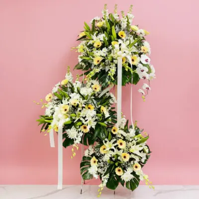A large floral arrangement of sympathy and funeral flowers featuring various blooms on a light pink background.