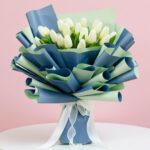 A bouquet of white tulips elegantly wrapped in blue and green ribbons, showcasing a fresh and vibrant floral arrangement.