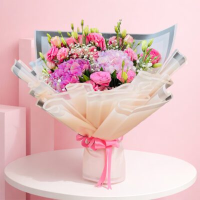 A vibrant hand bouquet with pink hydrangeas, eustoma, and baby breaths, complemented by greens, suitable for all occasions.
