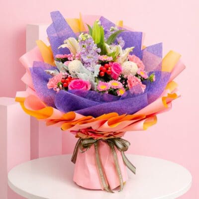 A vibrant bouquet of flowers wrapped in pink and purple paper, showcasing a mix of colors and textures.