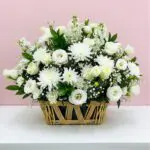 A basket filled with white flowers sits elegantly on a wooden table.