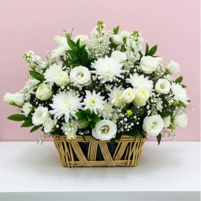 A basket filled with white flowers sits elegantly on a wooden table.