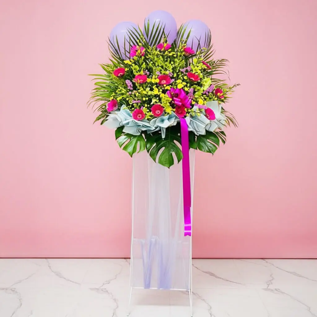 A grand opening flower stand featuring a vibrant arrangement of purple and pink Gerbera, orchids, and pompom flowers with balloons.