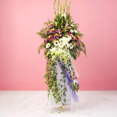 A large funeral flowers filled with a colorful arrangement of flowers set against a soft pink background.