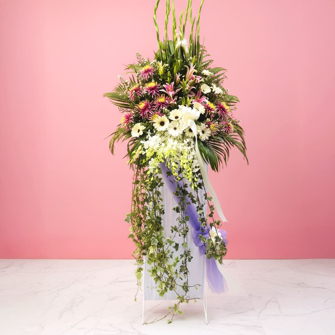 Memories in Bloom-05-59 A large funeral flowers filled with a colorful arrangement of flowers set against a soft pink background.