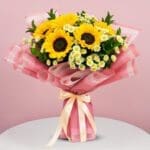 A bouquet featuring sunflowers and daisies in a white table