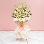 A vibrant bouquet of assorted flowers, including Eustoma and roses, in a vase against a soft pink background.